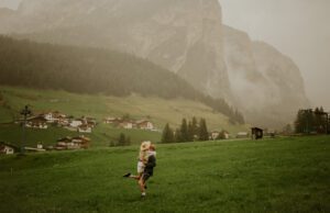 A couple spins around in a field in front of a mountain in the Dolomites, Italy 