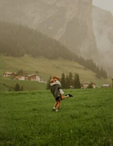 A couple spins around in a field in front of a mountain in the Dolomites, Italy 