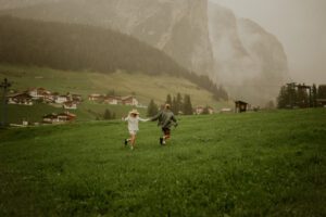 A couple runs around in a field in front of a mountain in the Dolomites, Italy 