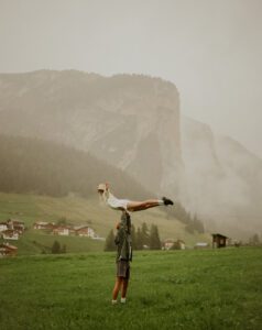 A man hols a woman over his head in front of a mountain in the Dolomites, Italy 
