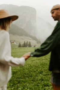 A couple holds hands and looks at each other in front of a mountain in the Dolomites, Italy. 