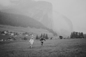 A couple runs around in a field in front of a mountain in the Dolomites, Italy 