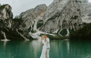 A bride and groom kiss in their wedding attire while looking out over Lago Di Braies in the Italian Dolomites