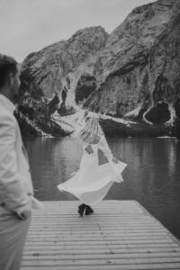A bride spins while groom watches while they stand on the dock at Lago Di Braies in the Italian Dolomites