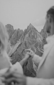 A black and white photo of a couple holding hands in front of Cadini Di Misurina in the Italian Dolomites