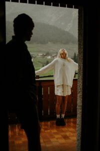 A couple stands on a porch in the rain in front of mountain in the Dolomites, Italy