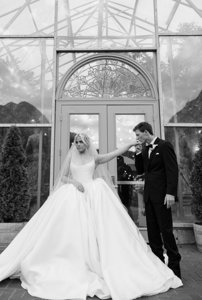 A bride and groom stand in front of a greenhouse solarium at La caille in Utah