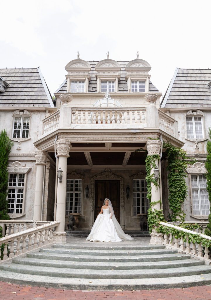 A bride standing in front of a French chateau wearing a Nicole + Felicia dress at La Caille Wedding Venue in Utah
