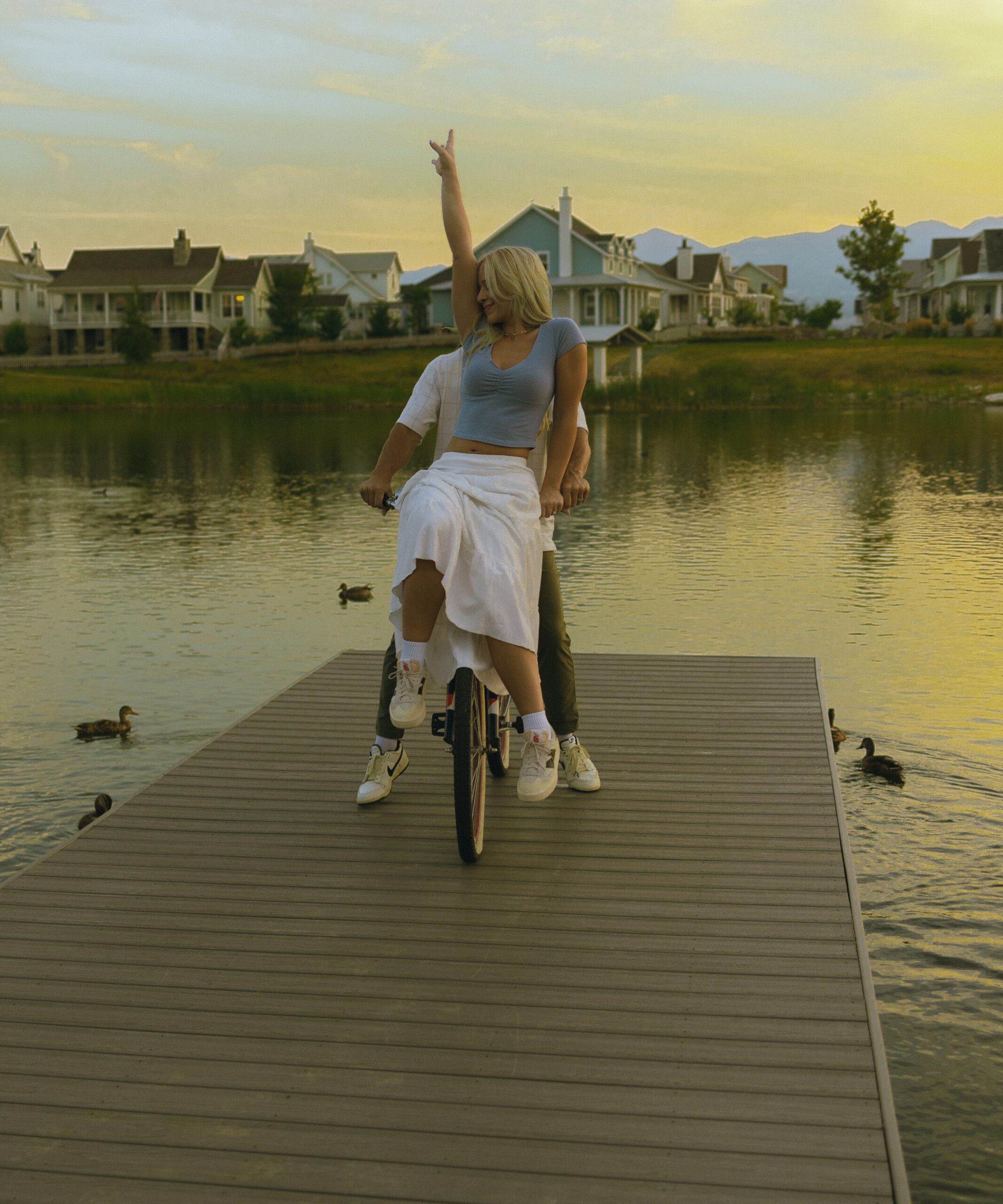 A couples rides a bike on a dock on a lake at sunset