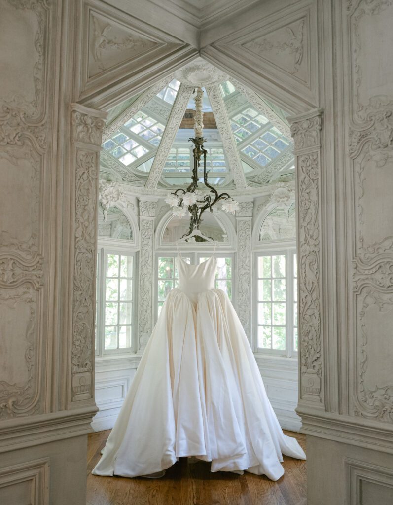 A Nicole Felicia dress hangs from a chandelier in a small room with detailed and ornate moulding at La Caille Wedding Venue in Utah