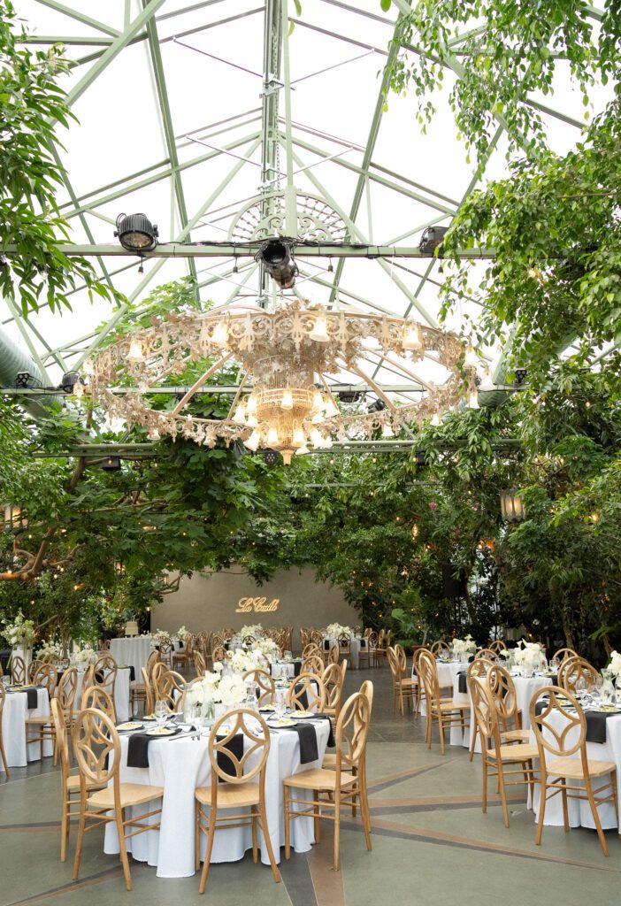 Greenhouse wedding reception setup at La Caille wedding venue in Utah, featuring chandeliers, hanging greenery, and elegant table settings
