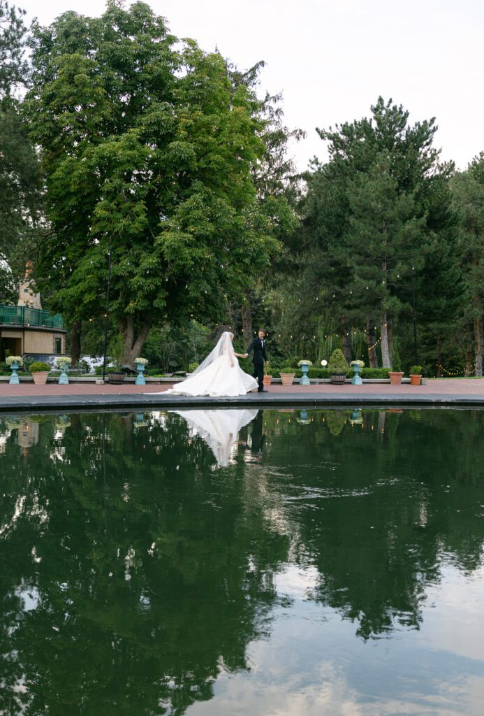A bride and groom walking next to a reflection pond with greenery all around at la caille wedding venue in Utah