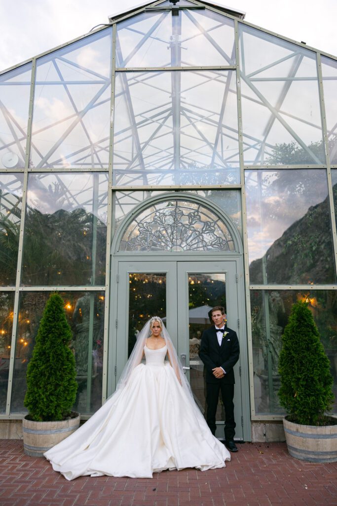 Bride and groom stands in front of a greenhouse solarium at La Caille Wedding Venue in Utah