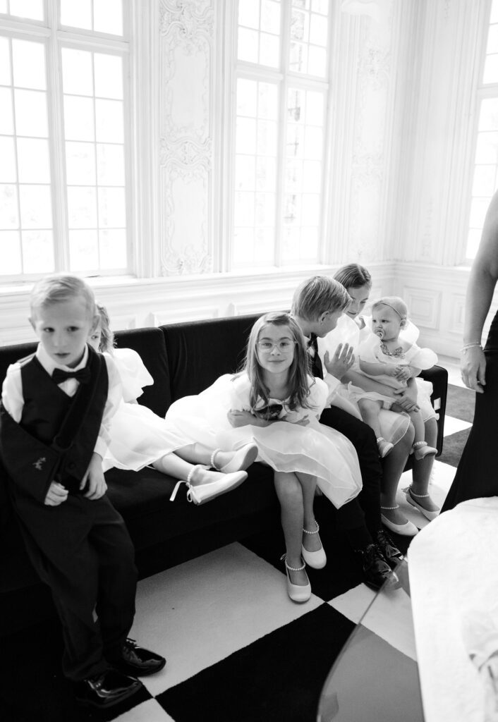 Kids dressed in wedding attire sit on a couch on a wedding day at La caille wedding venue in Utah