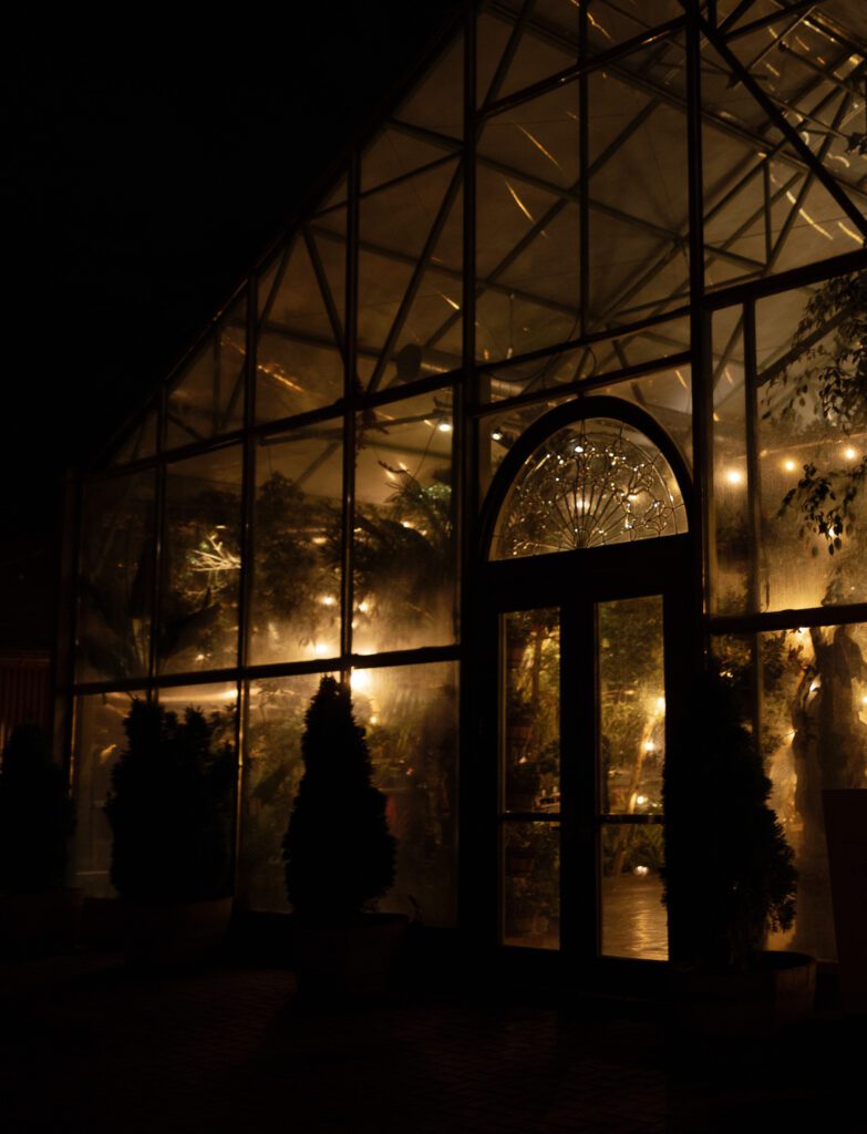 Evening view of the greenhouse at La Caille wedding venue in Utah, glowing with warm lights and glass architecture after sunset