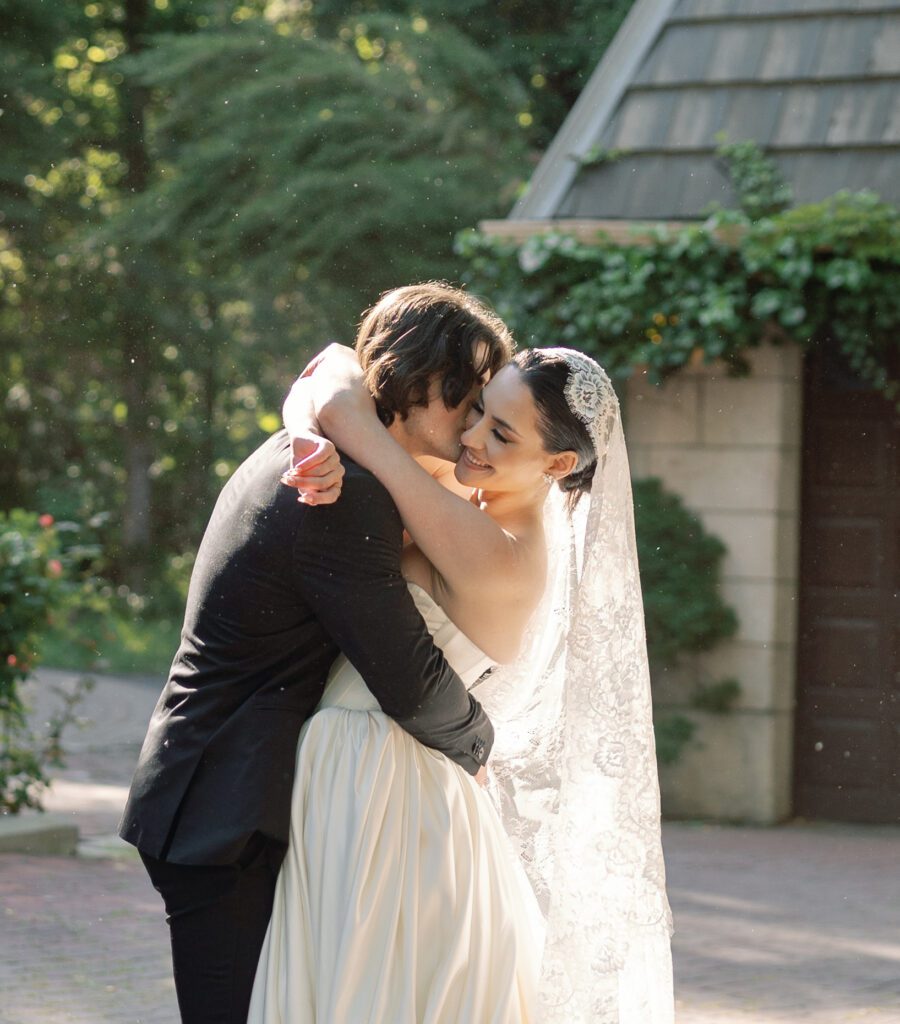 Bride and groom embracing during golden hour portraits at La Caille wedding venue in Utah, surrounded by lush greenery and historic stone buildings