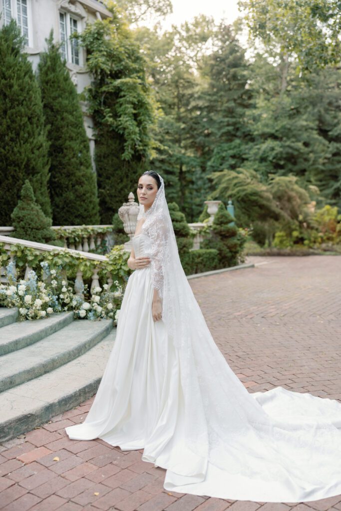 Bride in Basque waist gown and lace veil outside the chateau at a Spring La Caille wedding