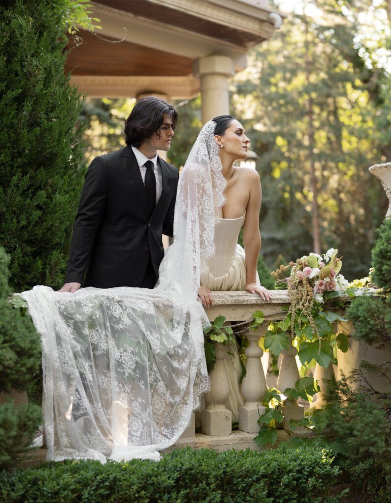 Bride in Basque waist gown with lace veil at La Caille chateau balcony in Utah