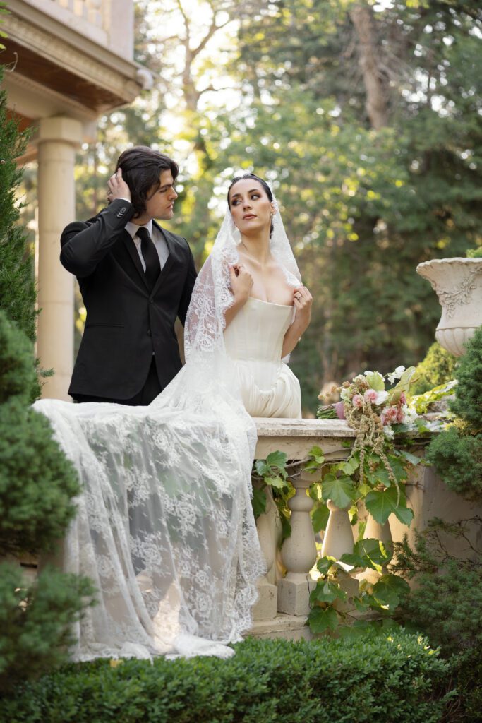 A bride and groom stand on the balcony of a French chateau at La Caille Wedding Venue in Utah