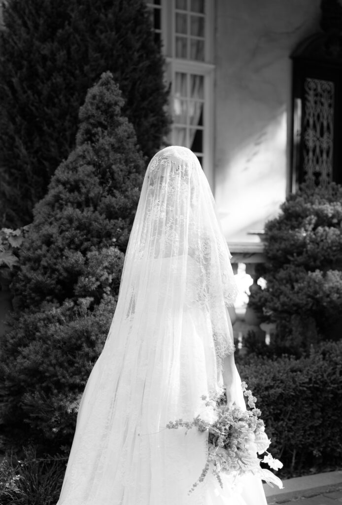 Bride with lace veil standing outside La Caille wedding venue in spring