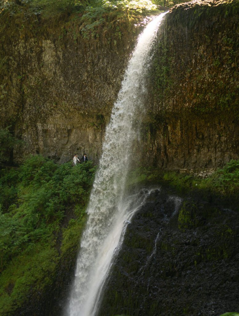bride and groom walking behind a waterfall at Silver Falls State Park in Oregon during an intimate elopement