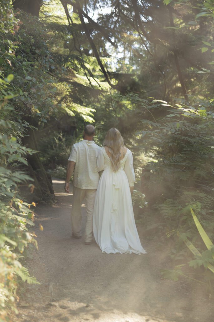 A bride and groom walking the short sands beach trail in Oswald West State Park surrounded by trees and hazy light