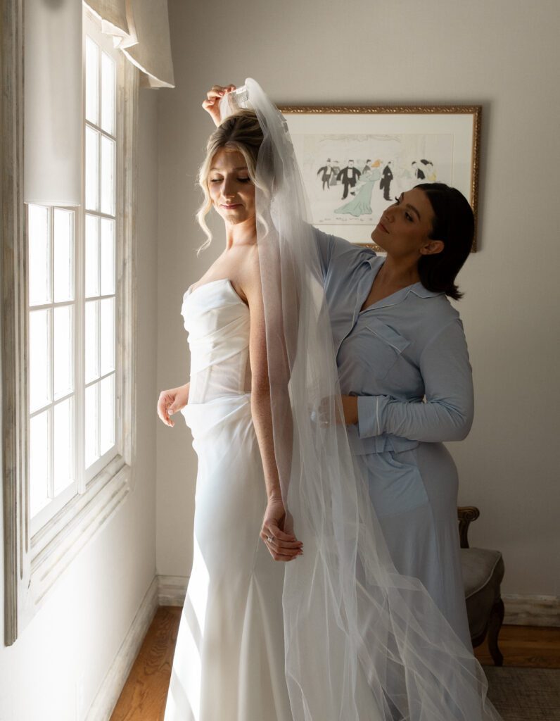 Bride getting ready with her sister beside a window at La Caille Utah
