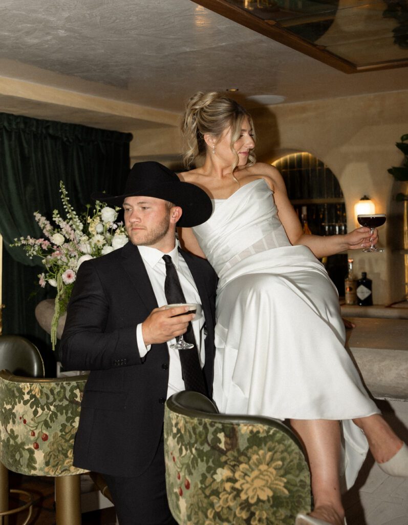 editorial photo of bride and groom sitting on a bar with drinks at la caille utah