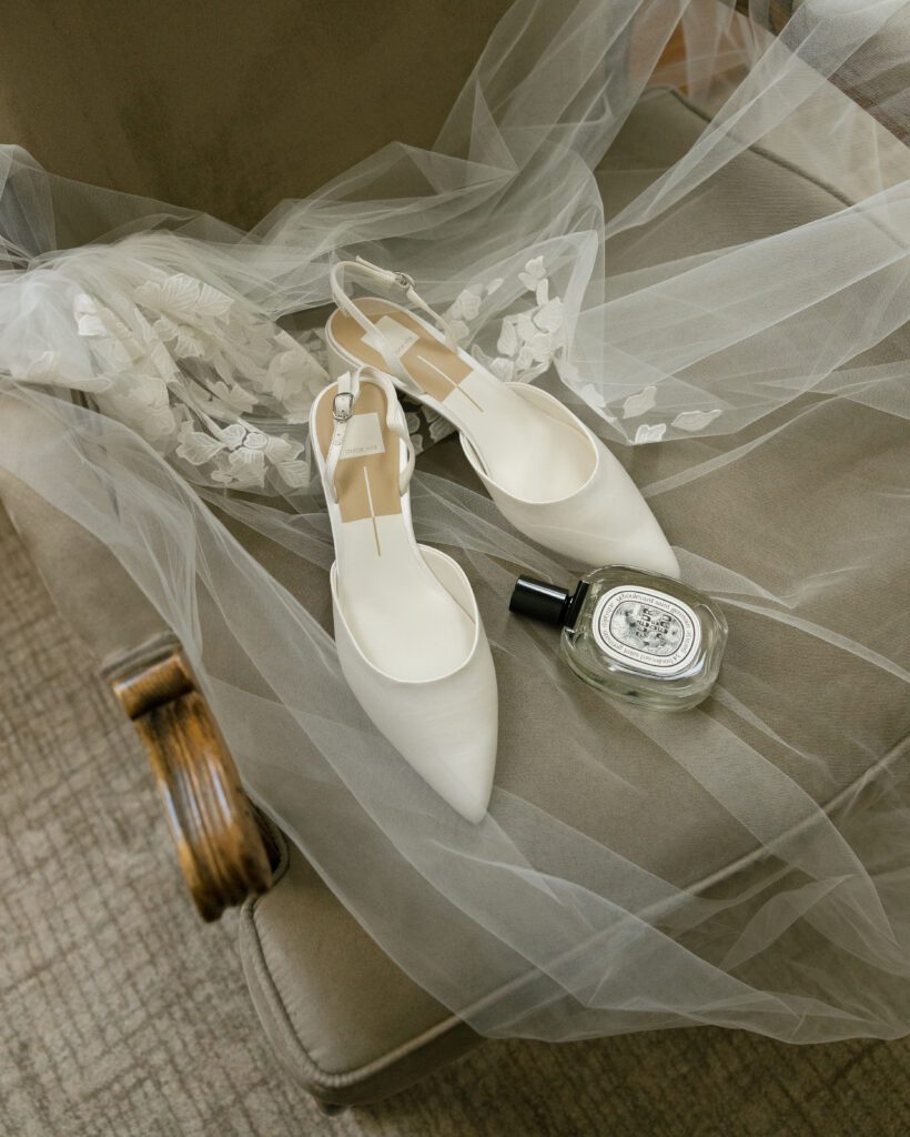 White bridal shoes and perfume photographed with a wedding veil